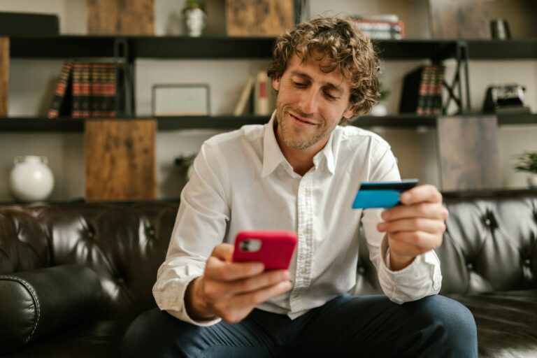A male patient sitting on a couch, holding a phone on one hand and a credit card on the other, presumably making a payment.